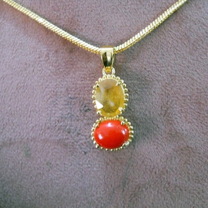 Könnte beinhalten: Eine goldene Kettenkette mit einem Anhänger mit zwei ovalen Edelsteinen. Der obere Edelstein ist ein hellgelber Citrin, der untere Edelstein ist eine leuchtend rote Koralle.