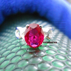 Puede incluir: Un anillo de plata con una gran piedra preciosa de color rosa brillante. El anillo está colocado sobre una superficie verde texturizada.