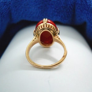 May include: A gold ring with an oval, reddish-orange gemstone. The ring has a detailed setting with a decorative design around the gemstone. The band is a simple, polished gold. The ring is likely a piece of jewellery.