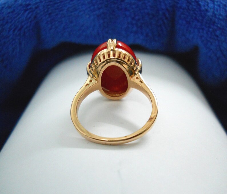 May include: A gold ring with an oval, reddish-orange gemstone. The ring has a detailed setting with a decorative design around the gemstone. The band is a simple, polished gold. The ring is likely a piece of jewellery.