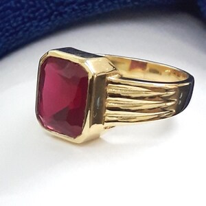 May include: A gold ring with a large, square-shaped, red gemstone.