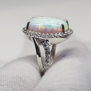 Può includere: Un anello d'argento con un grande opale ovale circondato da un'aureola di pietre più piccole e trasparenti.