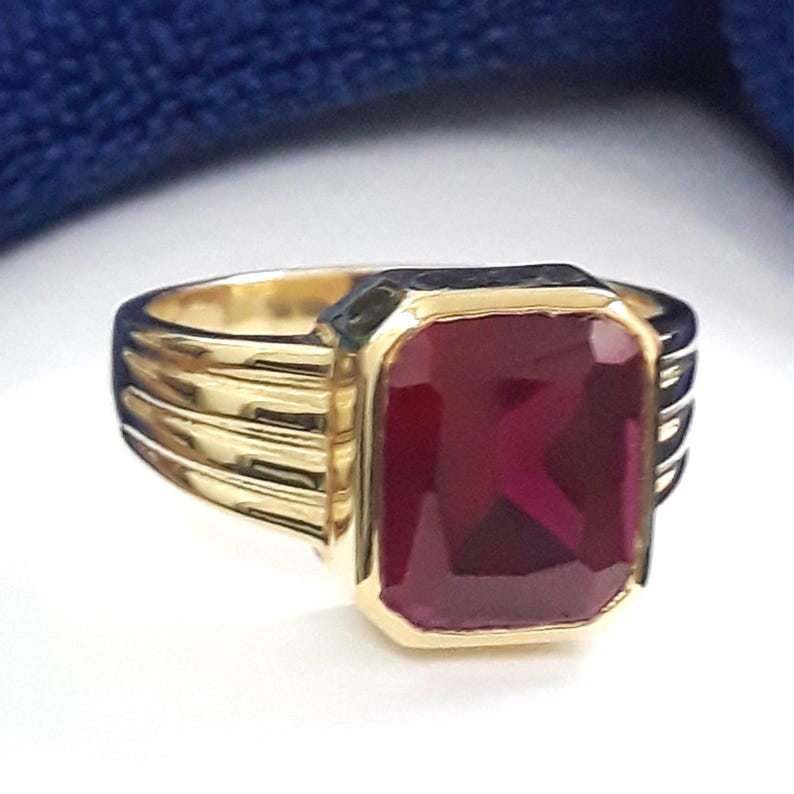 May include: A gold ring with a large, rectangular, dark red gemstone. The ring has a textured band.