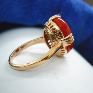 May include: Gold ring with a large, oval, red gemstone. The ring has a detailed gold setting with an openwork design around the gemstone. The band is smooth and polished, with a classic, elegant style.