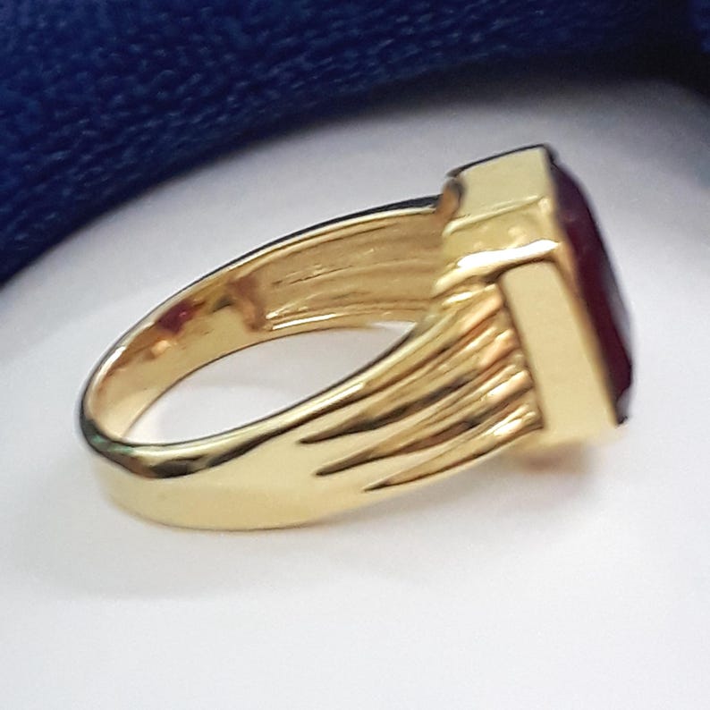 May include: A gold ring with a large, square, dark red gemstone. The ring has a textured band.