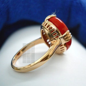 May include: A gold ring featuring a large, oval, red gemstone. The ring has an intricate, openwork design surrounding the gemstone and a polished band. The gemstone is a bright, striking red colour.