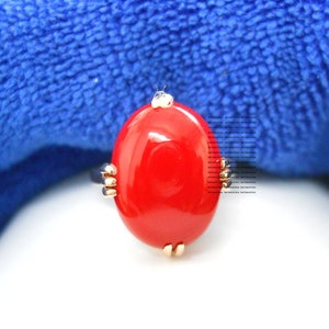 May include: A striking red oval ring with gold-coloured detailing. The ring showcases a large, glossy red stone set within a gold band. The design is simple yet eye-catching, suitable for everyday wear or special occasions.
