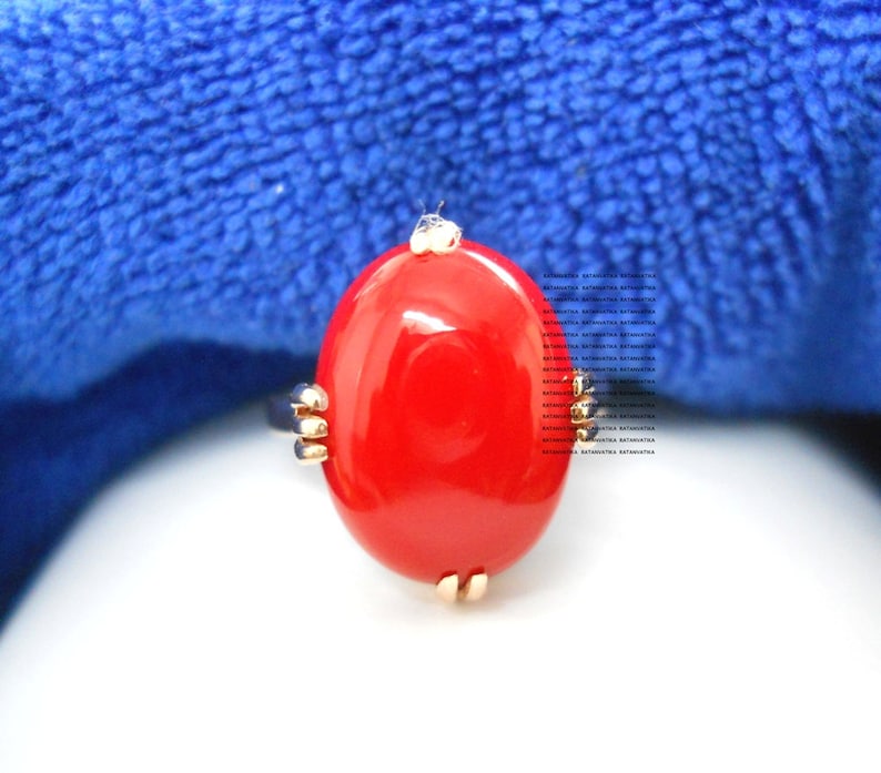 May include: A striking red oval ring with gold-coloured detailing. The ring showcases a large, glossy red stone set within a gold band. The design is simple yet eye-catching, suitable for everyday wear or special occasions.