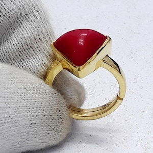 May include: A gold ring with a red gemstone. The ring is adjustable and has a square-shaped setting.