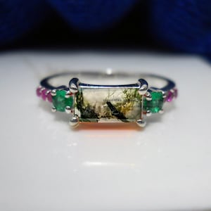 May include: A silver ring featuring a rectangular green and white stone set in the centre. The ring is accented with small pink and green stones.