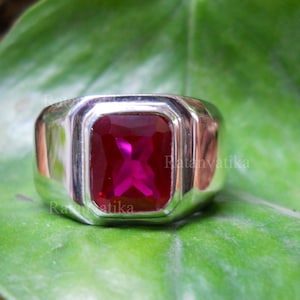 Peut inclure: Une bague en argent avec une grande pierre précieuse rectangulaire rose foncé sertie au centre.