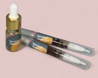 May include: Three clear glass bottles with gold lids and labels that say "lovekeys Beauty". The bottles contain a clear liquid with small pieces of dried flowers and herbs.