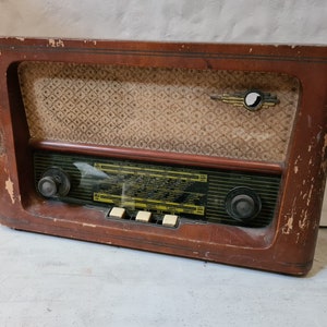 Könnte beinhalten: Ein Vintage-Holzradio mit einem braunen Holzkasten und einem schwarzen Lautsprechergitter. Das Radio hat ein Zifferblatt mit verschiedenen Stationen und zwei Knöpfe für Lautstärke und Abstimmung. Das Radio hat einen verblassten, gemusterten Stoff, der den Lautsprecher bedeckt.