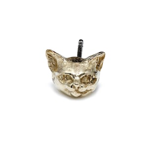 Op de afbeelding: Een zilverkleurige deurknop in de vorm van een kattenkop met een zwarte schroef.