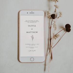 May include: A white smartphone screen displays a wedding invitation for Olivia & Matthew. The invitation includes the date, time, and location of the wedding: Saturday, June 21, 2023 at 2:00 PM, One Whitehall Place, London.