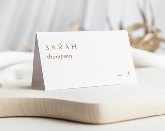 May include: White place card with gold lettering. The name "SARAH thompson" is printed on the card, along with the number "no. 1".