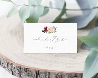 May include: White wedding place card with a floral design in shades of pink and burgundy. The card reads "Amanda Davidson" and "Table 1".