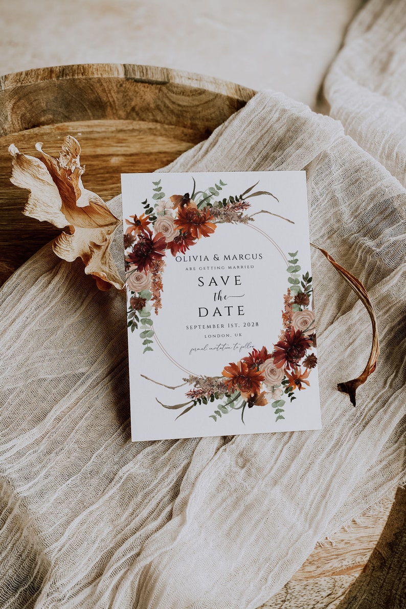 Peut inclure: Carte de sauvegarde de la date avec une couronne de fleurs dans des tons de rouge, orange et blanc. Le texte indique "Olivia & Marcus se marient. Sauvegarde de la date. 1er septembre 2028. Londres, Royaume-Uni. Invitation formelle &agrave; suivre."