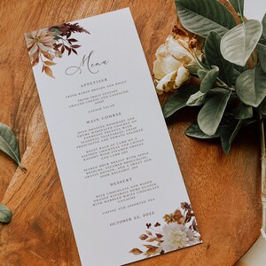 May include: A fall-themed menu card with a floral design in shades of brown, orange, and white. The menu lists appetizers, main courses, and desserts. The text on the card reads "Menu", "Appetizer", "Fresh Baked Breads and Rolls", "Fresh Fruit Station", "Grilled Cheese and Gazpacho Soup", "Caesar Salad", "Main Course", "Oven Roasted Rosemary and Thyme Marinated Chicken on Parmesan Polenta with Seasonal Vegetables, Crisp Prosciutto and Tomato Veloute", "Roast Rack of Lamb on a Saffron Chickpeas and Crives Ragout with Steamed Greens and Lamb Jus", "Seared Duck Breast with Apple Brioche, Steamed Broccoli, Gratin Potato, and a Sweet and Sour Balsamic Jus", "Dessert", "Milk Chocolate and Blood Orange Bavarois Dome Glazed with Marbled White Chocolate Ganache", "Coffee and Assorted Tea", and "October 22, 2022".