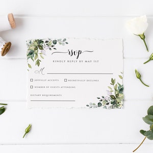Puede incluir: Una tarjeta RSVP blanca con acentos de follaje verde y flores. La tarjeta tiene un RSVP escrito a mano en letra negra y el texto "Kindly reply by May 1st". Hay casillas de verificaci&oacute;n para "Joyfully accepts" y "Regretfully declines". Hay una l&iacute;nea para "Number of guests attending" y "Dietary requirements".