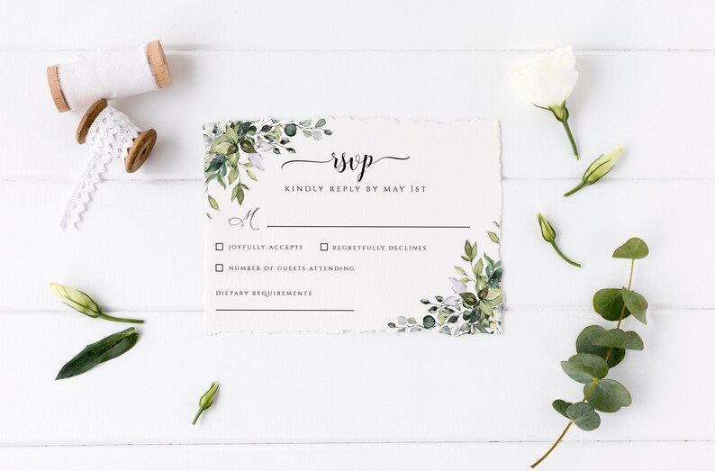 Puede incluir: Una tarjeta RSVP blanca con acentos de follaje verde y flores. La tarjeta tiene un RSVP escrito a mano en letra negra y el texto "Kindly reply by May 1st". Hay casillas de verificaci&oacute;n para "Joyfully accepts" y "Regretfully declines". Hay una l&iacute;nea para "Number of guests attending" y "Dietary requirements".