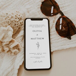 May include: A white wedding invitation on a smartphone screen with a floral design. The invitation reads "The pleasure of your company is requested at the wedding of Olivia & Matthew. Saturday, June 21, 2023 at 2:00 PM. One Whitehall Place, London. Reception to follow."