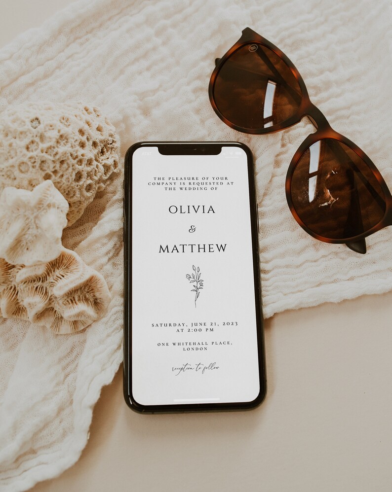 May include: A white wedding invitation on a smartphone screen with a floral design. The invitation reads "The pleasure of your company is requested at the wedding of Olivia & Matthew. Saturday, June 21, 2023 at 2:00 PM. One Whitehall Place, London. Reception to follow."