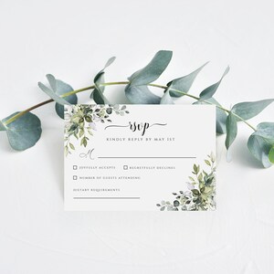Puede incluir: Tarjeta RSVP blanca con borde floral de acuarela verde. El texto dice "RSVP" en cursiva y "Por favor, responda antes del 1 de mayo". La tarjeta tiene casillas de verificaci&oacute;n para "Acepta con gusto" y "Rechaza con pesar" y espacio para "N&uacute;mero de invitados que asistir&aacute;n" y "Requisitos diet&eacute;ticos".