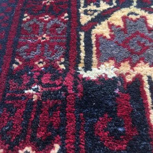 Puede incluir: Primer plano de una alfombra roja, negra y crema con un patr&oacute;n geom&eacute;trico. La alfombra tiene un aspecto desgastado y vintage.
