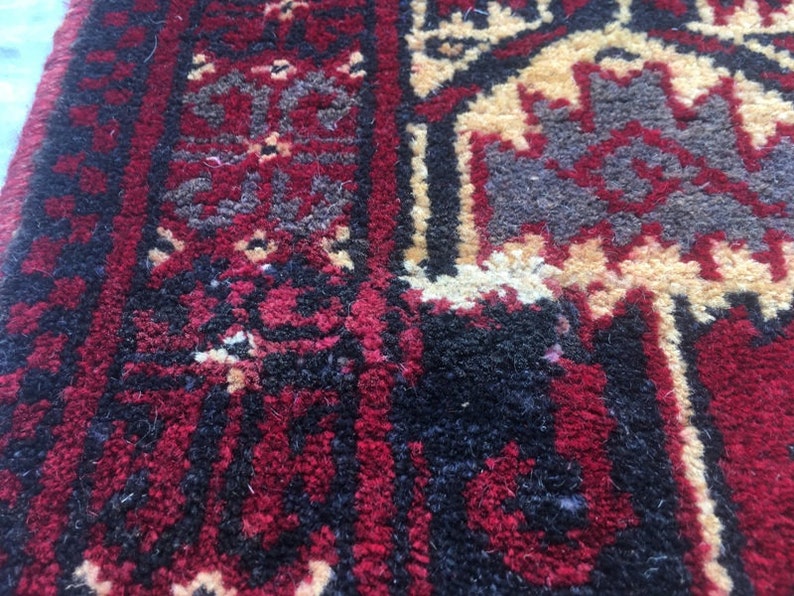 Puede incluir: Primer plano de una alfombra roja, negra y crema con un patr&oacute;n geom&eacute;trico. La alfombra tiene un aspecto desgastado y vintage.