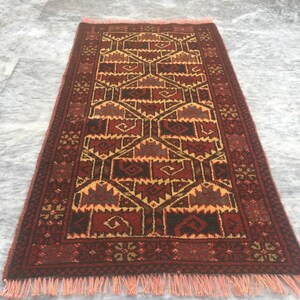 Puede incluir: Una alfombra roja, marr&oacute;n y amarilla con un dise&ntilde;o geom&eacute;trico. La alfombra tiene un borde de flecos.