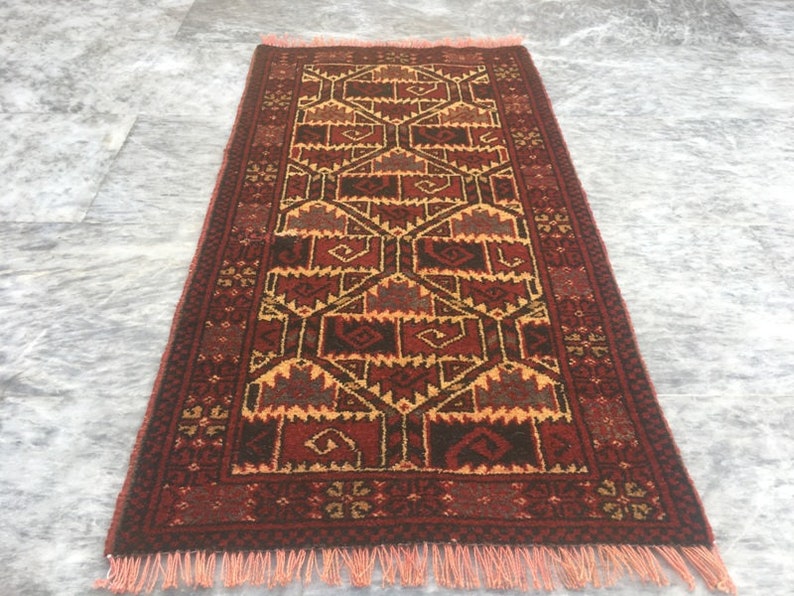 Puede incluir: Una alfombra roja, marr&oacute;n y amarilla con un dise&ntilde;o geom&eacute;trico. La alfombra tiene un borde de flecos.