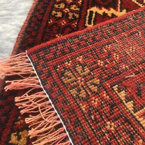 Puede incluir: Una alfombra roja, negra y beige con un borde de flecos. La alfombra tiene un dise&ntilde;o geom&eacute;trico y est&aacute; hecha de lana.
