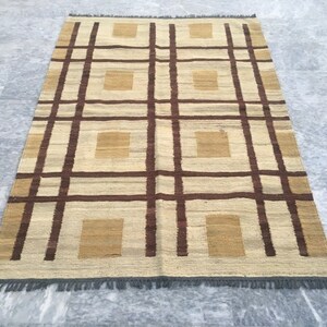 May include: A woven rug with a geometric pattern of brown and beige squares and stripes. The rug has a fringe border.