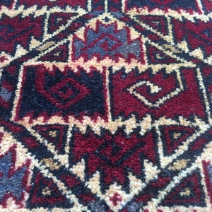 Puede incluir: Primer plano de una alfombra roja, negra y crema con un patr&oacute;n geom&eacute;trico. La alfombra tiene un dise&ntilde;o tradicional con detalles intrincados.