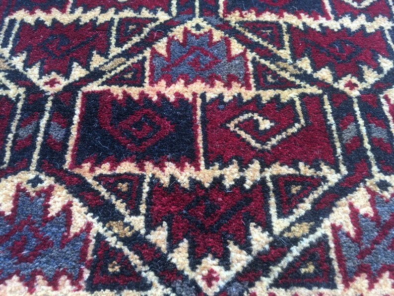 Puede incluir: Primer plano de una alfombra roja, negra y crema con un patr&oacute;n geom&eacute;trico. La alfombra tiene un dise&ntilde;o tradicional con detalles intrincados.