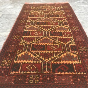 Puede incluir: Una alfombra roja, marr&oacute;n y amarilla con un dise&ntilde;o geom&eacute;trico. La alfombra tiene un borde con flecos.