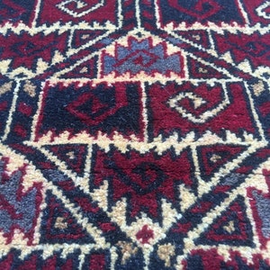 Puede incluir: Primer plano de una alfombra roja, negra y crema con un patr&oacute;n geom&eacute;trico. La alfombra tiene un dise&ntilde;o tradicional con detalles intrincados.