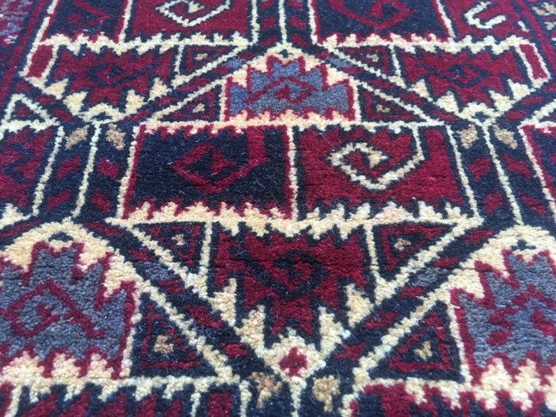 Puede incluir: Primer plano de una alfombra roja, negra y crema con un patr&oacute;n geom&eacute;trico. La alfombra tiene un dise&ntilde;o tradicional con detalles intrincados.