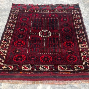 May include: A red and black rug with a geometric pattern. The rug has a fringe border and is made of wool.