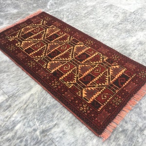 Puede incluir: Una alfombra roja, naranja y negra con un borde de flecos. La alfombra tiene un dise&ntilde;o geom&eacute;trico con un patr&oacute;n de diamantes.