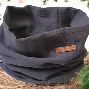 Könnte beinhalten: Ein dunkelgrauer, handgefertigter, Stoff-Halswärmer oder Schal. Der Stoff ist weich und texturiert. Der Halswärmer hat ein braunes Leder-Etikett mit dem Wort "Handmade" darauf.