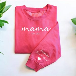 May include: Pink sweatshirt with the text "mama est. 2023" on the front and "Josephine Luca & Emil" with a heart on the sleeve.