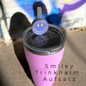 Könnte beinhalten: Ein rosa Becher mit schwarzem Deckel und einem blauen Smiley-Strohhalm-Aufsatz. Der Text "Smiley Trinkhalm-Aufsatz" ist auf der Seite des Bechers aufgedruckt. Der Hintergrund zeigt ein farbenfrohes Graffiti-Design.