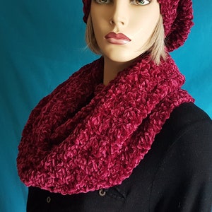 May include: A burgundy crocheted infinity scarf and matching beanie hat. The scarf is made of a soft, fuzzy yarn and is perfect for keeping warm in the winter.
