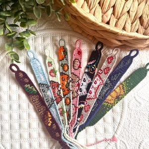 May include: A collection of handmade friendship bracelets in various colors and patterns. Designs include floral, geometric, and animal motifs. Each bracelet has a loop at one end and braided threads at the other.