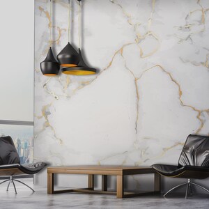 May include: Three black pendant lights hang from the ceiling above a wooden coffee table and two black leather chairs in a modern living room with a white marble wall with gold veins.