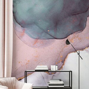 May include: A pink and teal abstract watercolour print with gold accents. The print is displayed on a wall behind a black shelf with books and a lamp.