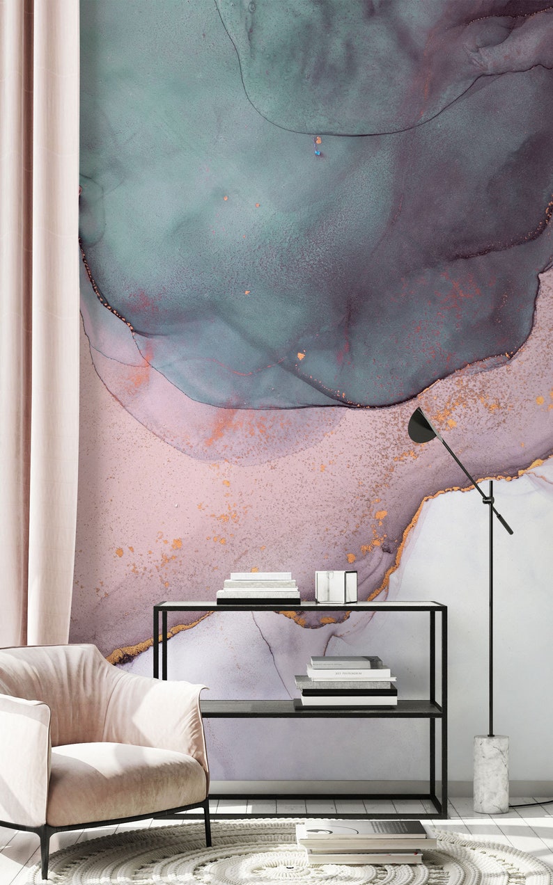 May include: A pink and teal abstract watercolour print with gold accents. The print is displayed on a wall behind a black shelf with books and a lamp.