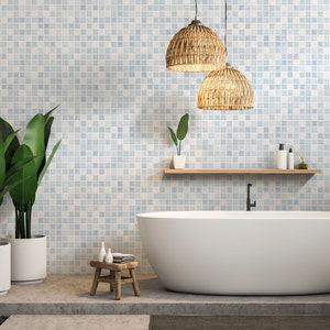 May include: A white bathtub with a black faucet sits in a bathroom with light blue mosaic tile walls. Two woven pendant lights hang from the ceiling. Two potted plants are on the left side of the image. A small wooden stool with a white towel sits in front of the bathtub.